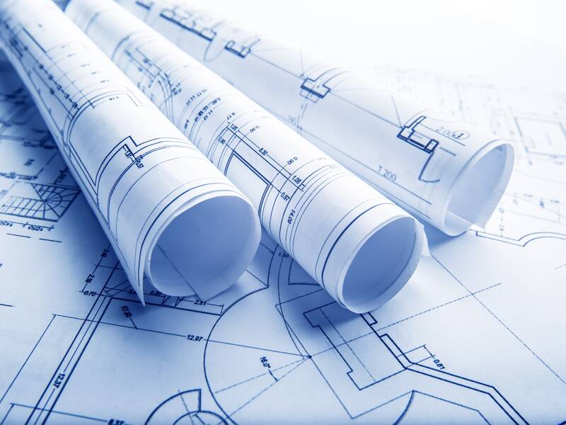 Three blueprints rolled up on top of another spread-out blueprint.