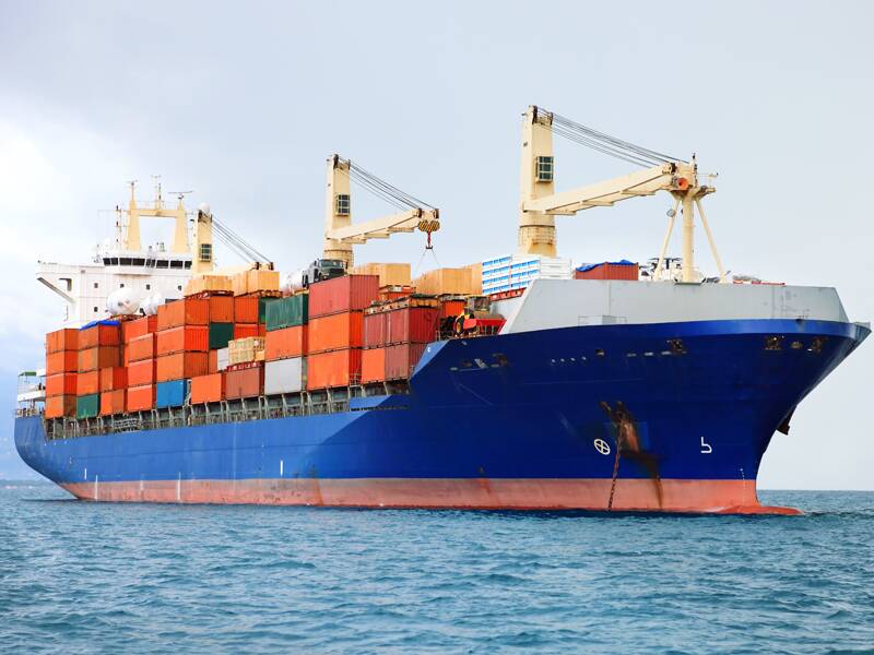 Cargo ship with dozens of freight containers on deck at sea.