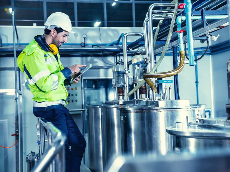 Man wearing a yellow high-res jacket in a factory surrounded by stainless steel appliances.